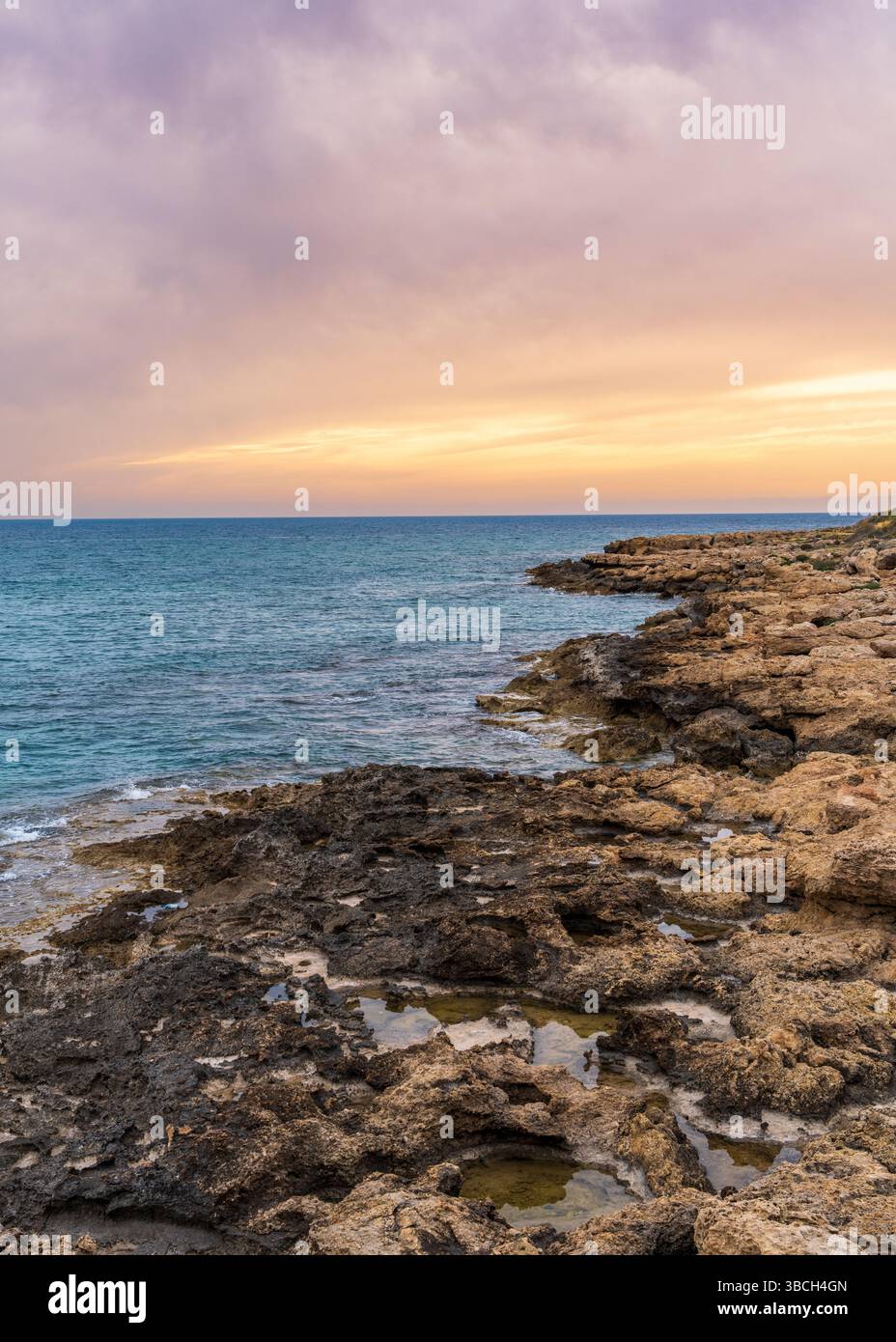 Costa rocciosa al tramonto vicino a Paphos, Cipro. Pittoresco paesaggio marino mediterraneo con scogliere aspre, calda luce del tramonto. Perfetto per viaggi e natura Foto Stock
