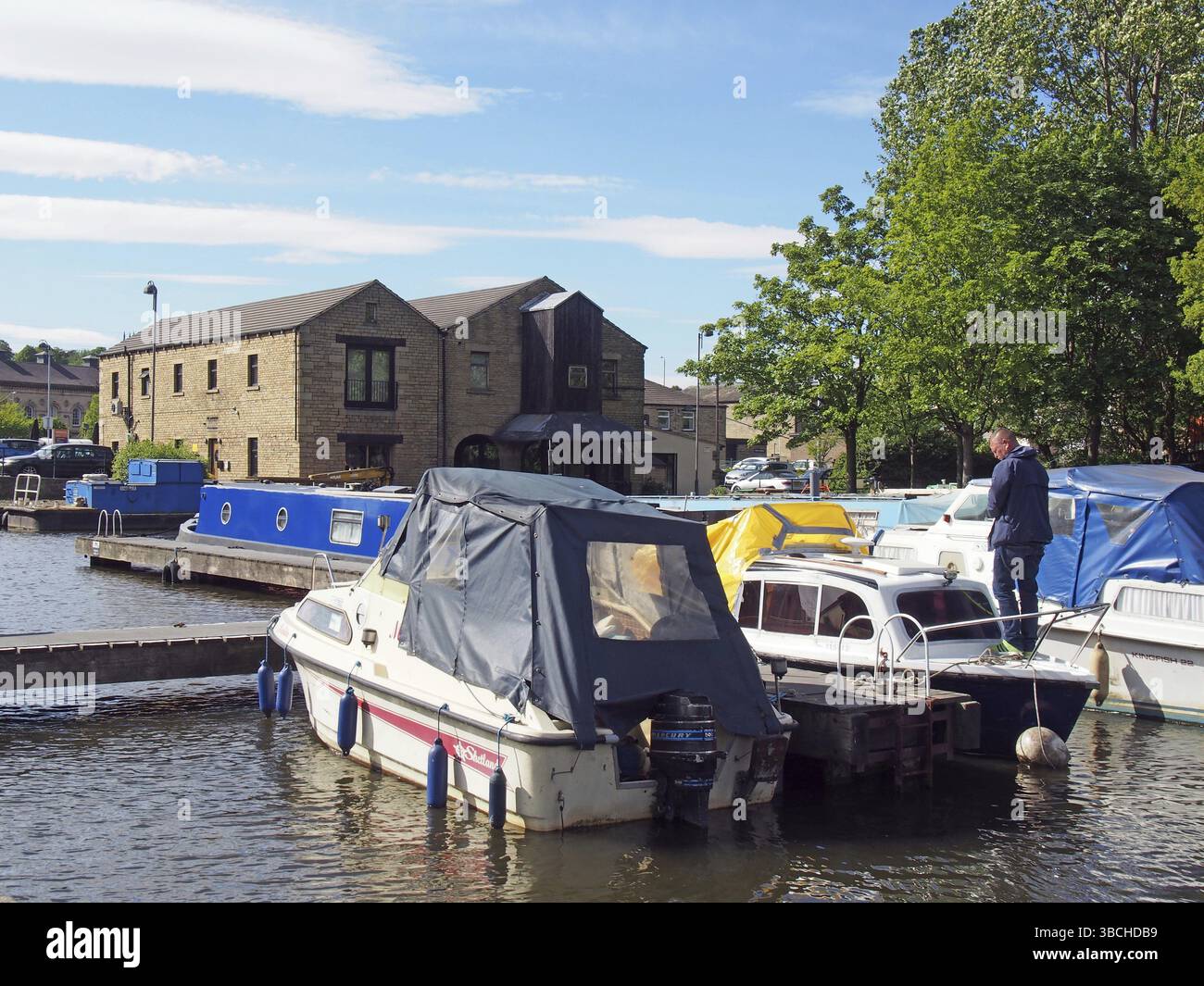 Brighouse, West yorkshire, regno unito: 24 maggio 2017: Un uomo su una casa galleggiante circondato da chiatte ormeggiate nel bacino di brighouse e ormeggi sulla CA Foto Stock