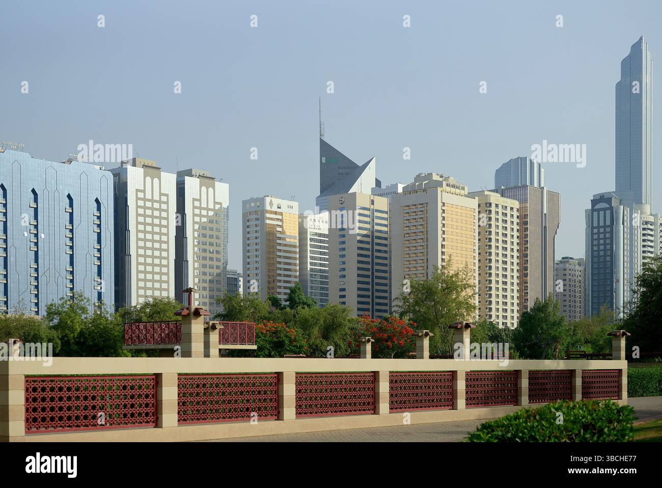 Skyline della città con moderni grattacieli e vegetazione verde sotto un cielo azzurro. Abu Dhabi, Emirati Arabi Uniti Foto Stock