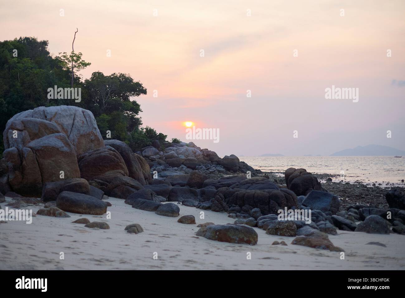 Una tranquilla spiaggia rocciosa al tramonto con morbidi cieli pastello e alberi lontani. Thailandia Foto Stock