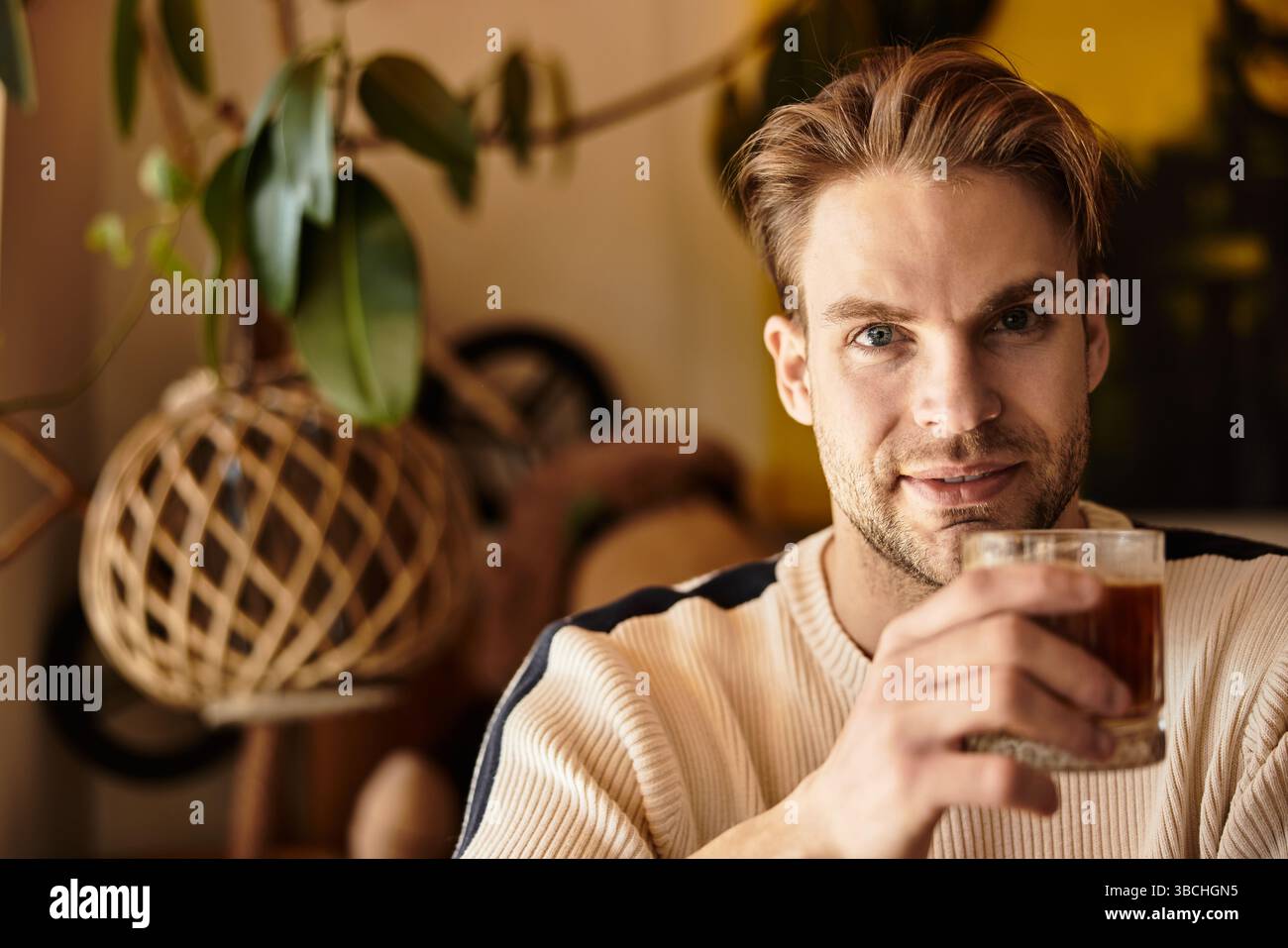Un uomo affascinante si rilassa con un drink in mano, godendosi l'atmosfera calda e il decor. Foto Stock