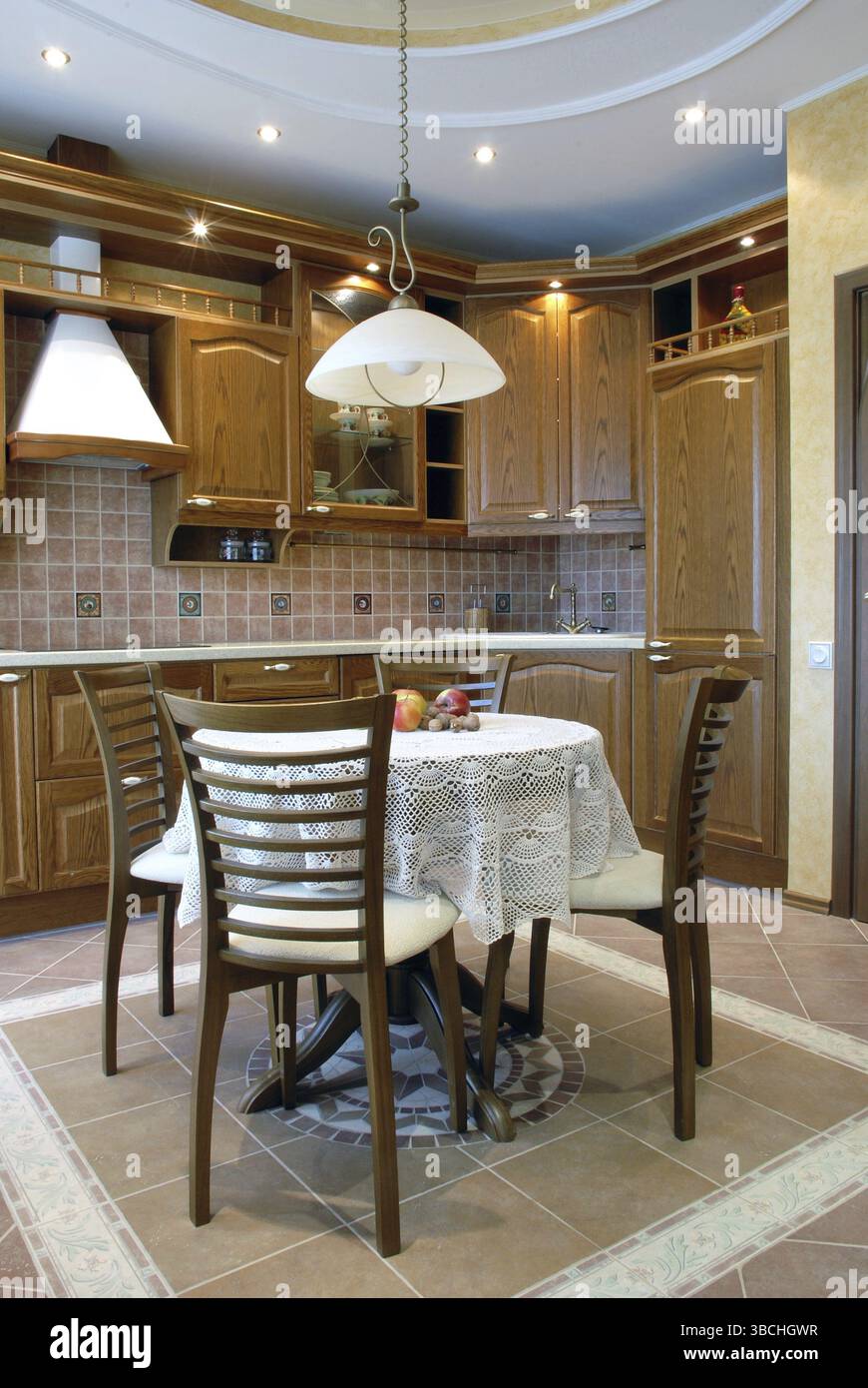 Cucina accogliente: Armadietti in noce, tavolo rotondo ricoperto da un bellissimo tovagliolo bianco all'uncinetto con mele rubicunte su di esso, quattro sedie, divano basso Foto Stock