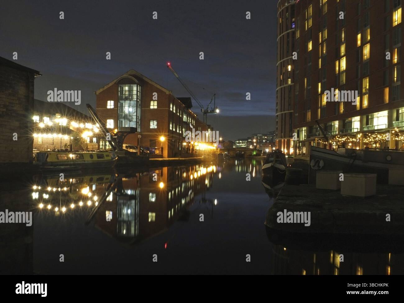 Una vista notturna del canale di leeds con l'ingresso al molo dei granai, i moderni sviluppi sul mare e la luce riflessa nelle barche ormeggiate sull'acqua Foto Stock