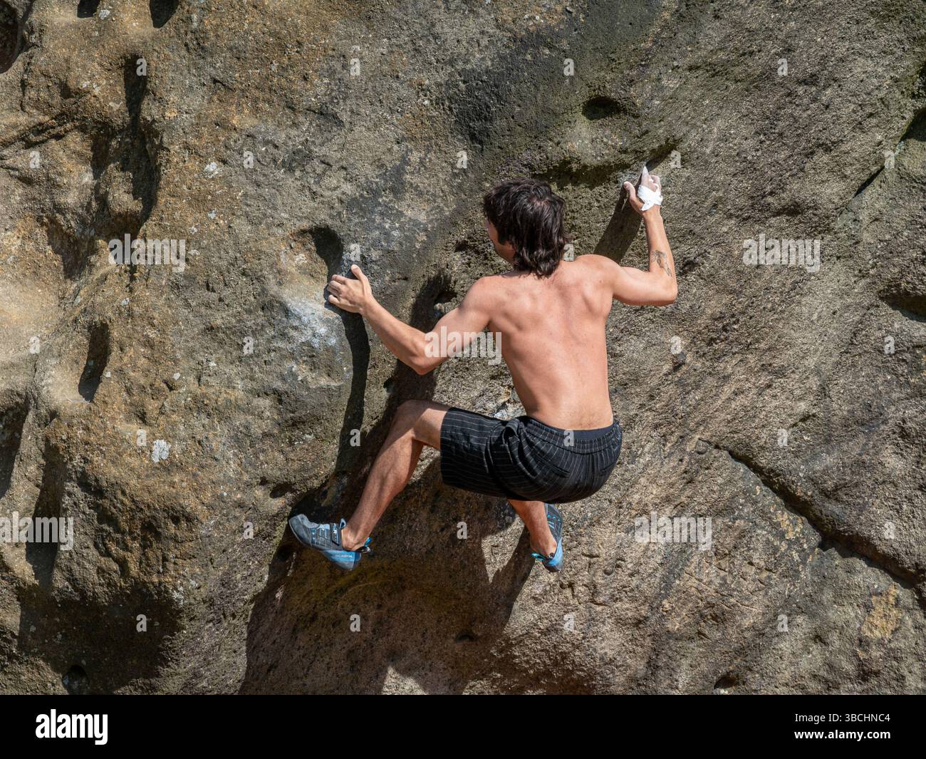 In una giornata di sole, un alpinista maschio che si arrampica sul Calf, parte delle Cow and Calf Rocks a Ilkley Moor nel West Yorkshire. Foto Stock
