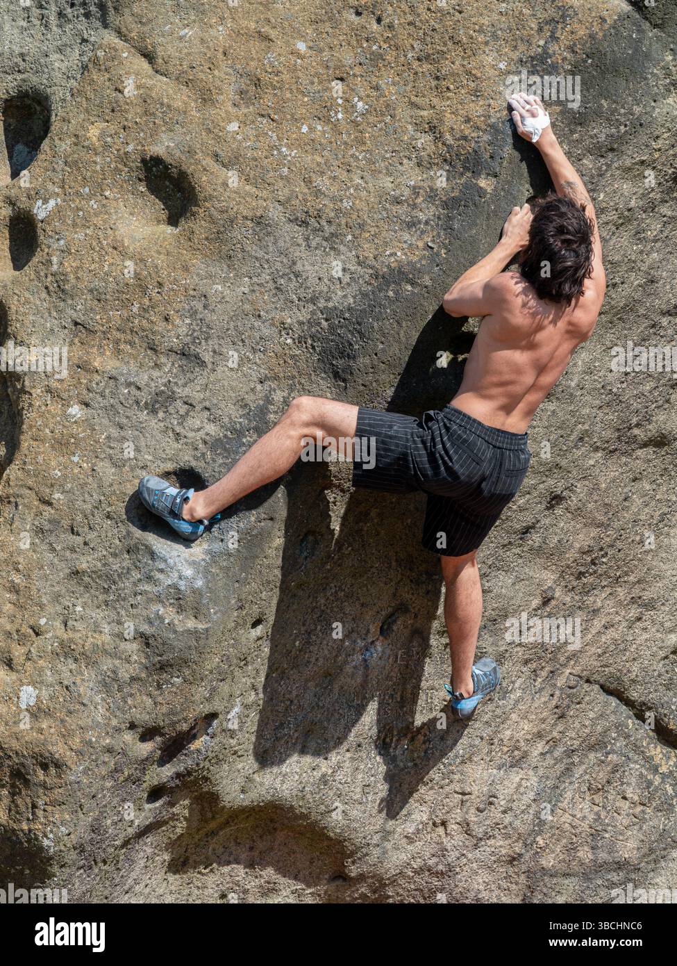 In una giornata di sole, un alpinista maschio che si arrampica sul Calf, parte delle Cow and Calf Rocks a Ilkley Moor nel West Yorkshire. Foto Stock
