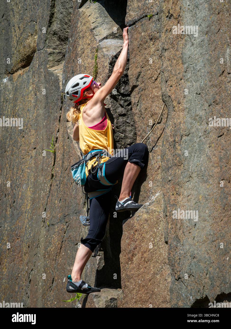 Una arrampicatrice femmina sale sul volto della mucca, la più grande delle rocce mucca e vitello a Ilkley Moor, nello Yorkshire, in una giornata di sole Foto Stock