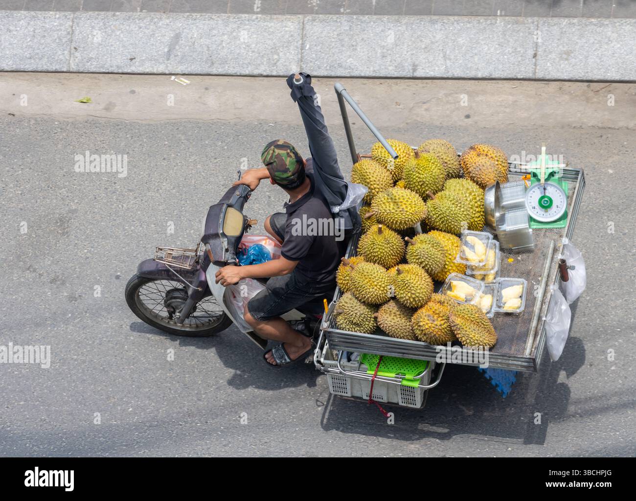 Un venditore su una motocicletta trasporta un carrello carico di duriani freschi e frutta confezionata, Vietnam. Foto Stock