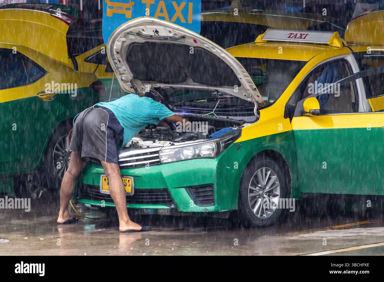 Il meccanico ripara il motore del taxi in caso di pioggia alla stazione dei taxi della città Foto Stock