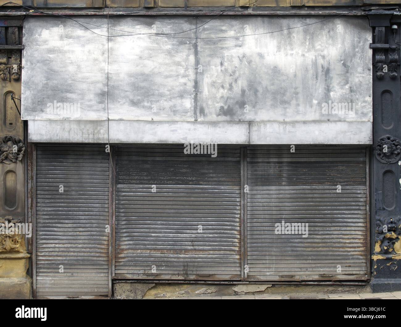 La facciata di un negozio abbandonato su una strada con persiane chiuse in metallo arrugginite sopra l'ingresso del negozio e la porta Foto Stock