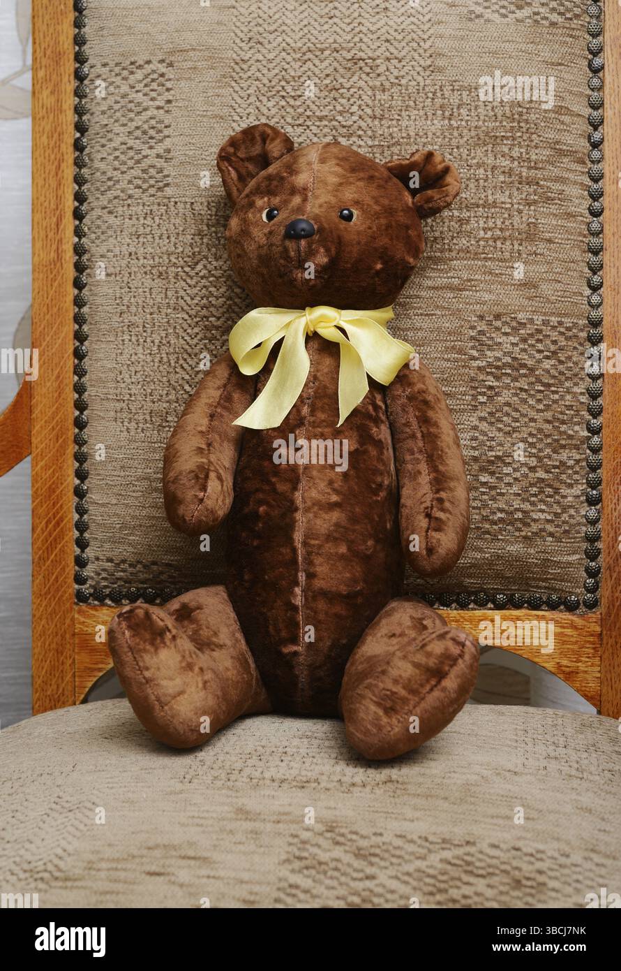 Orsacchiotto squallido con un arco giallo sul collo seduto in una vecchia poltrona vintage Foto Stock