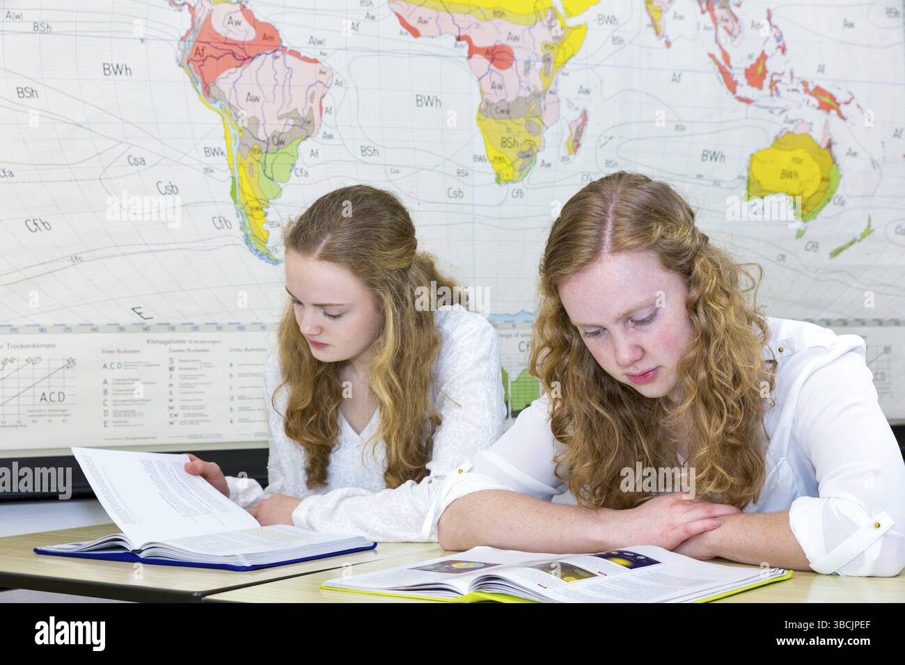 Due caucasica sorelle adolescenti studiano nella parte anteriore della parete mondo grafico in aula sulla scuola Foto Stock