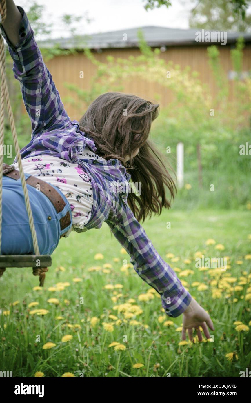 Ragazza su un'altalena che si allunga qui al braccio fino a un prato Foto Stock