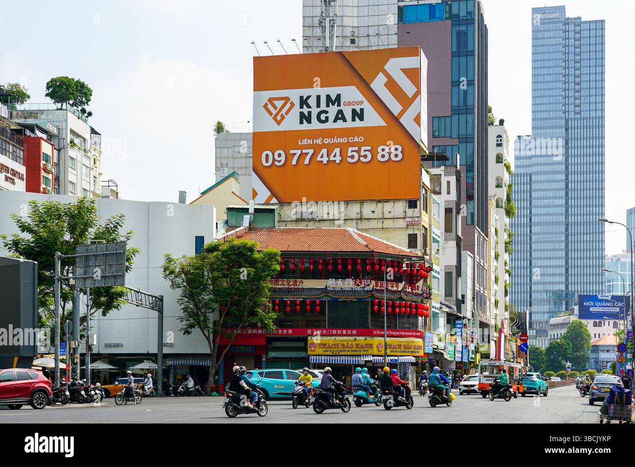Ho chi Minh City, Vietnam - 16 marzo 2025: Strada trafficata con cartelloni colorati e moderni grattacieli che svettano sopra l'architettura tradizionale Foto Stock