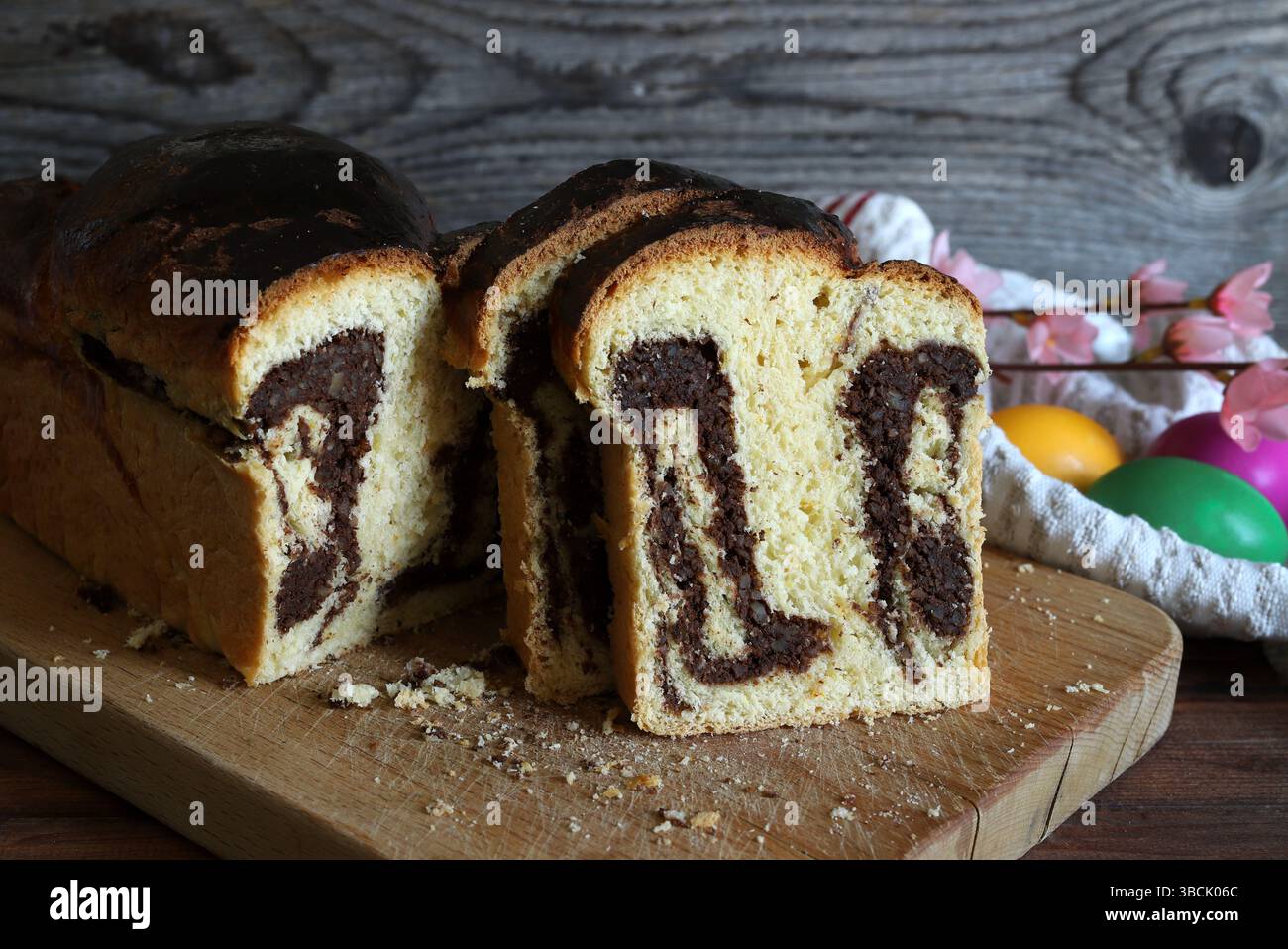 Cozonac. Taglio del tradizionale pane dolce rumeno di Pasqua su un tagliere di legno e uova di Pasqua sullo sfondo. Vacanze gastronomiche dell'Europa orientale. Foto Stock