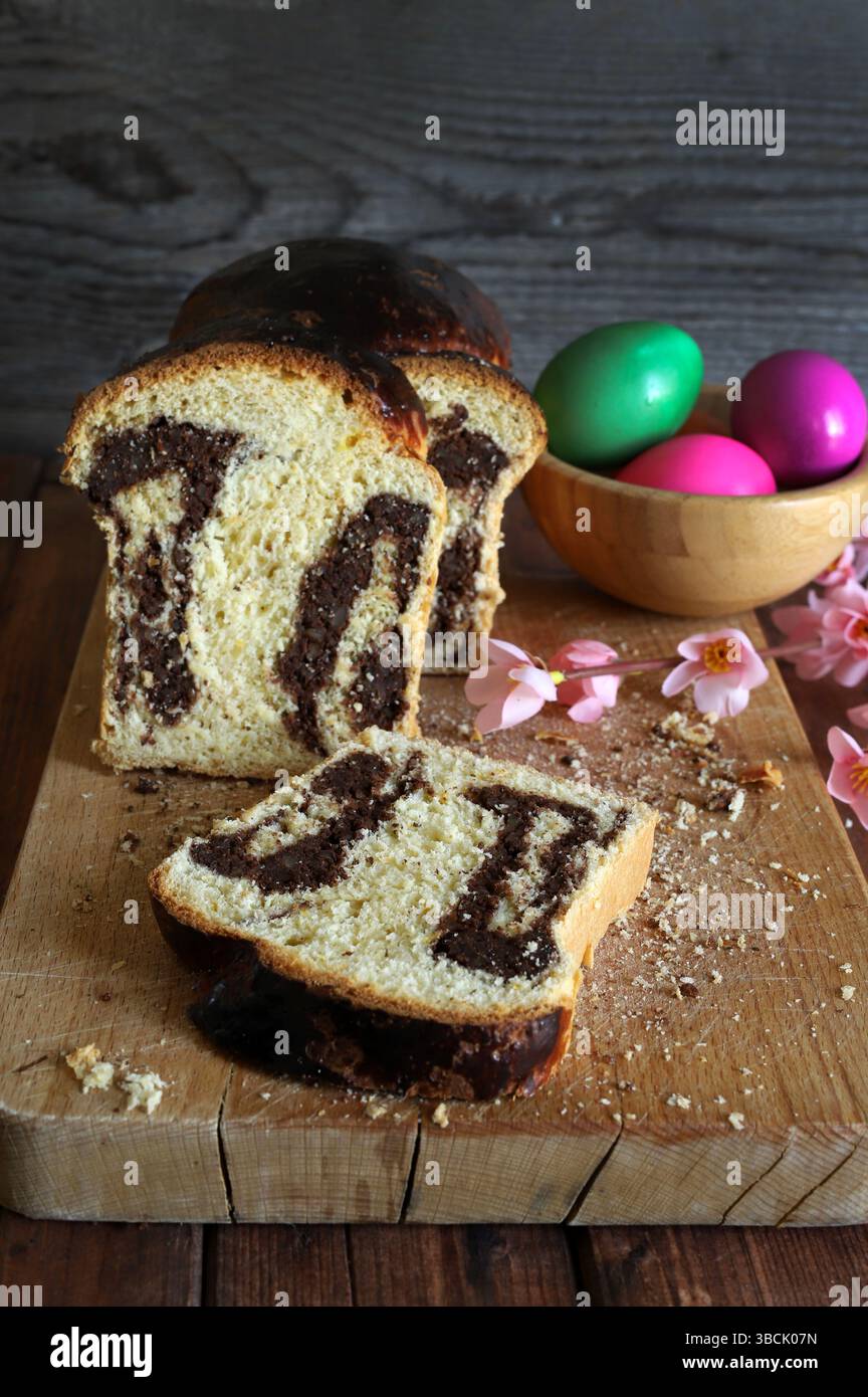 Cozonac. Taglio del tradizionale pane dolce rumeno di Pasqua su un tagliere di legno e uova di Pasqua sullo sfondo. Vacanze gastronomiche dell'Europa orientale. Foto Stock