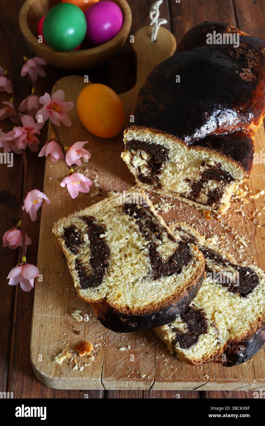 Cozonac. Taglio del tradizionale pane dolce rumeno di Pasqua su un tagliere di legno e uova di Pasqua sullo sfondo. Vacanze gastronomiche dell'Europa orientale. Foto Stock