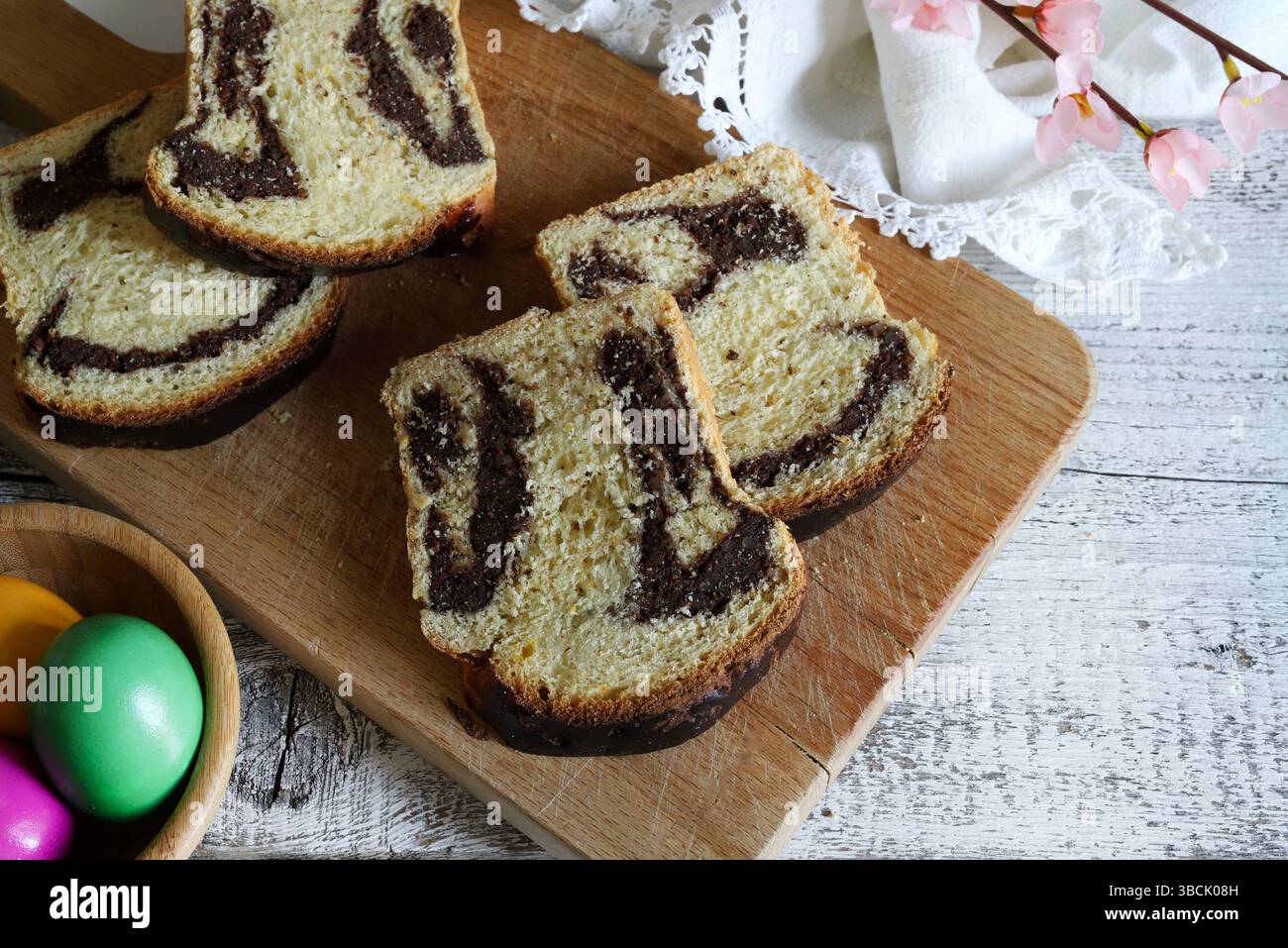 Cozonac. Taglio del tradizionale pane dolce rumeno di Pasqua su un tagliere di legno e uova di Pasqua sullo sfondo. Vacanze gastronomiche dell'Europa orientale. Foto Stock