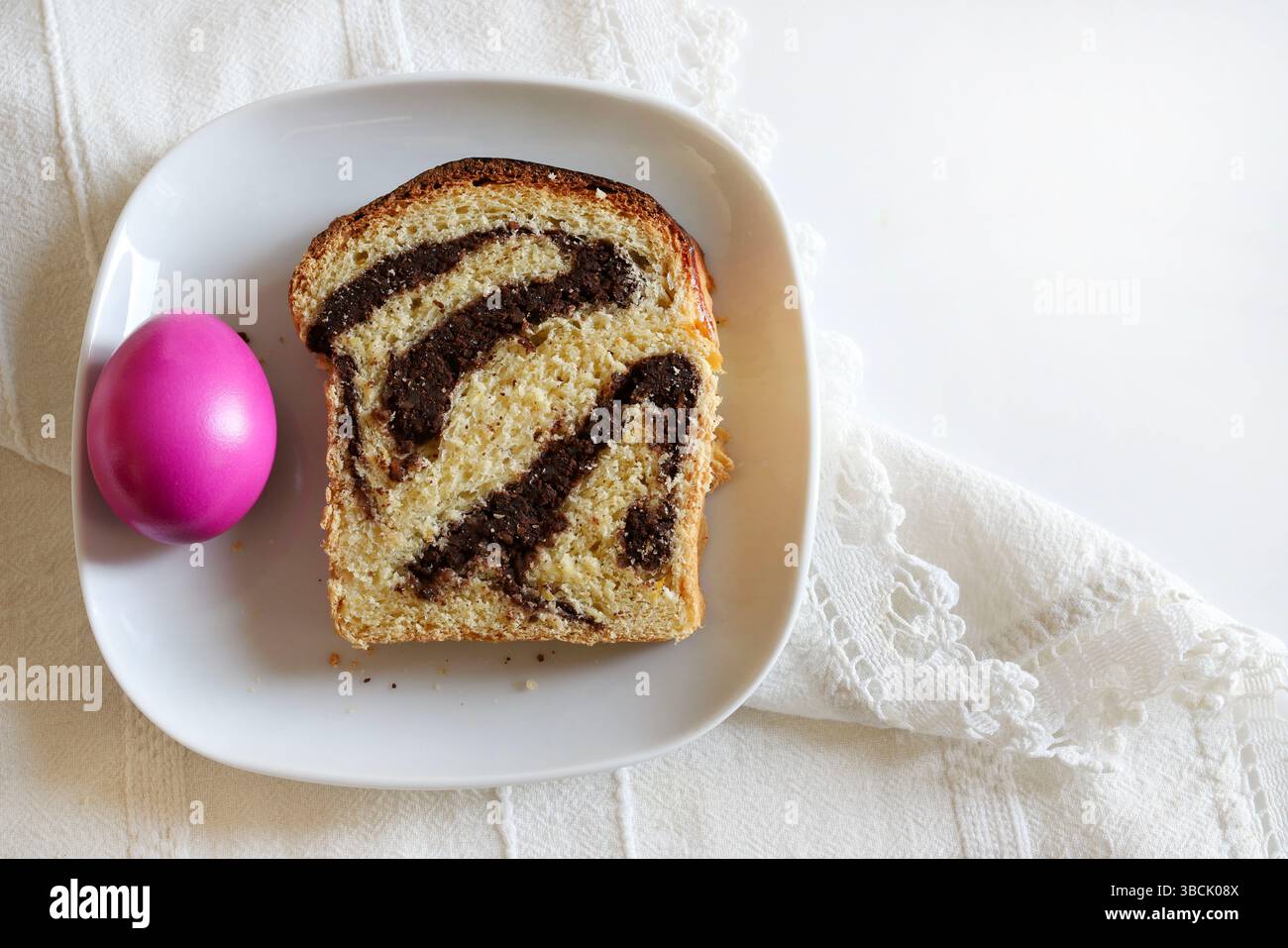 Cozonac, tradizionale dessert rumeno di pane dolce pasquale. Una fetta di pane dolce e uova di Pasqua su sfondo bianco. Concetto di vacanza di Pasqua. Foto Stock