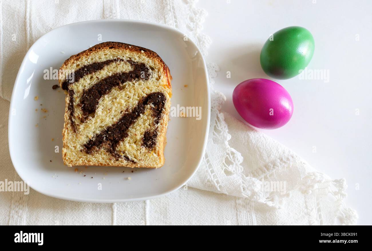 Cozonac, tradizionale dessert rumeno di pane dolce pasquale. Una fetta di pane dolce e uova di Pasqua su sfondo bianco. Concetto di vacanza di Pasqua. Foto Stock