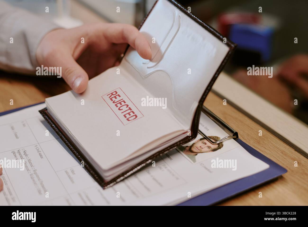 Passaporto di apertura a mano che mostra un grande timbro rosso rifiutato sulla pagina accompagnato da alcuni documenti personali e appunti con documenti sul tavolo Foto Stock