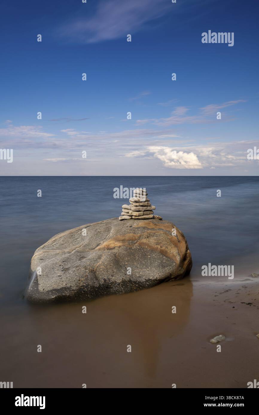 Un corno di roccia meditativo sulla cima di un masso con l'oceano a lunga esposizione e il cielo sullo sfondo Foto Stock