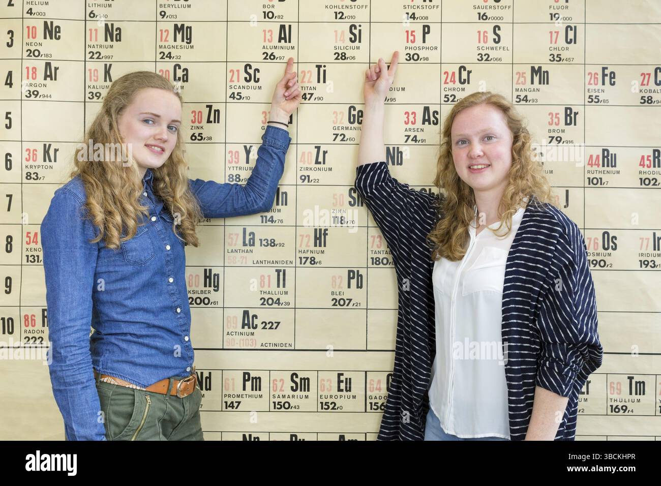 Due studentesse punto al tabellone a parete tabella periodica nella lezione di Chimica Foto Stock
