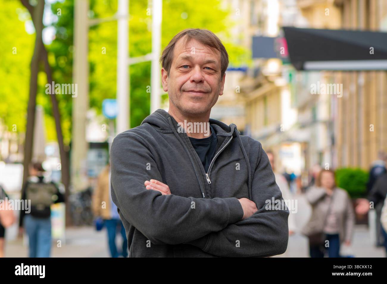 Un uomo sorridente per strada, tra pedoni e architettura urbana è l'immagine di un passante o di un abitante della città Foto Stock