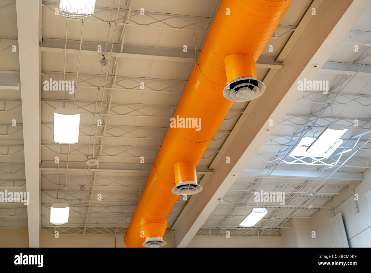 HVAC per interni, sistemi meccanici, condotto arancione, tubi di ventilazione, con diffusore bianco, appeso al soffitto di un grande spazio aperto. Foto Stock