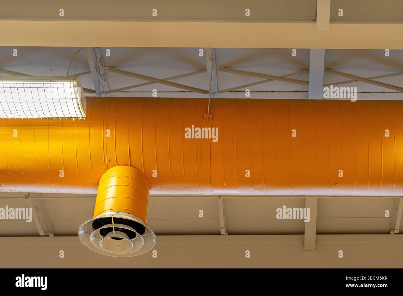 HVAC per interni, sistemi meccanici, condotto arancione, tubi di ventilazione, con diffusore bianco, appeso al soffitto di un grande spazio aperto. Foto Stock