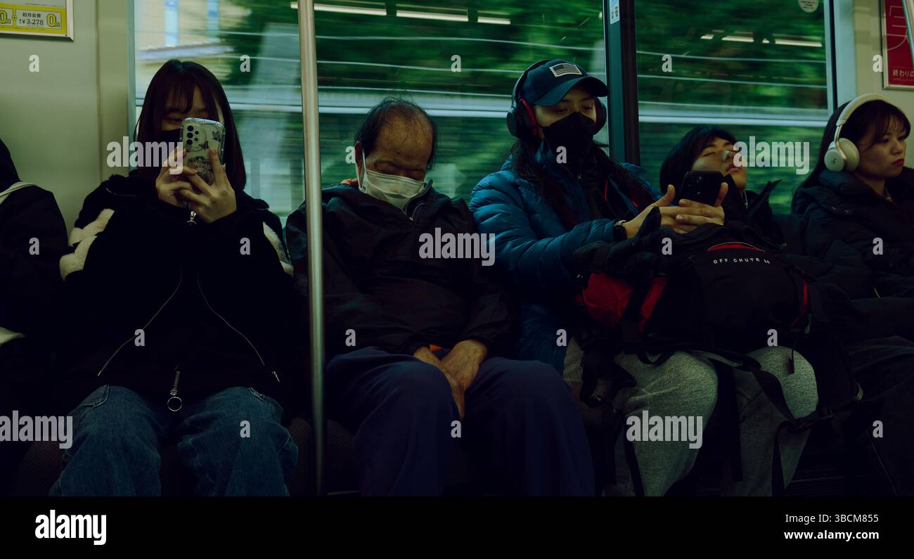 Momenti tranquilli sulla metropolitana di Tokyo, dove gli schermi si intrattengono e dormono durante il tragitto mattutino Foto Stock