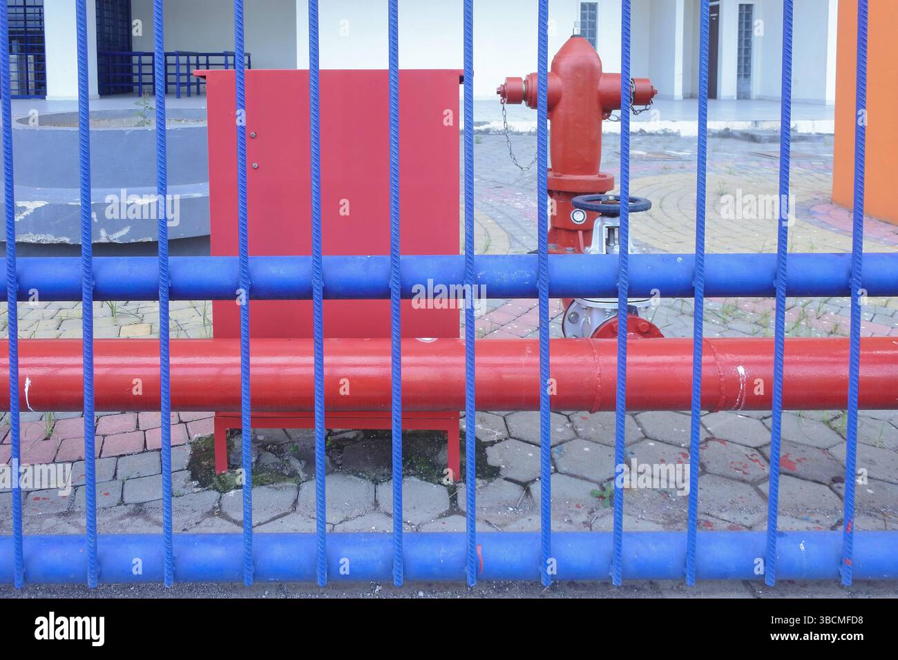 idrante rosso, dietro una recinzione di ferro dipinta di blu nel cortile di un edificio Foto Stock