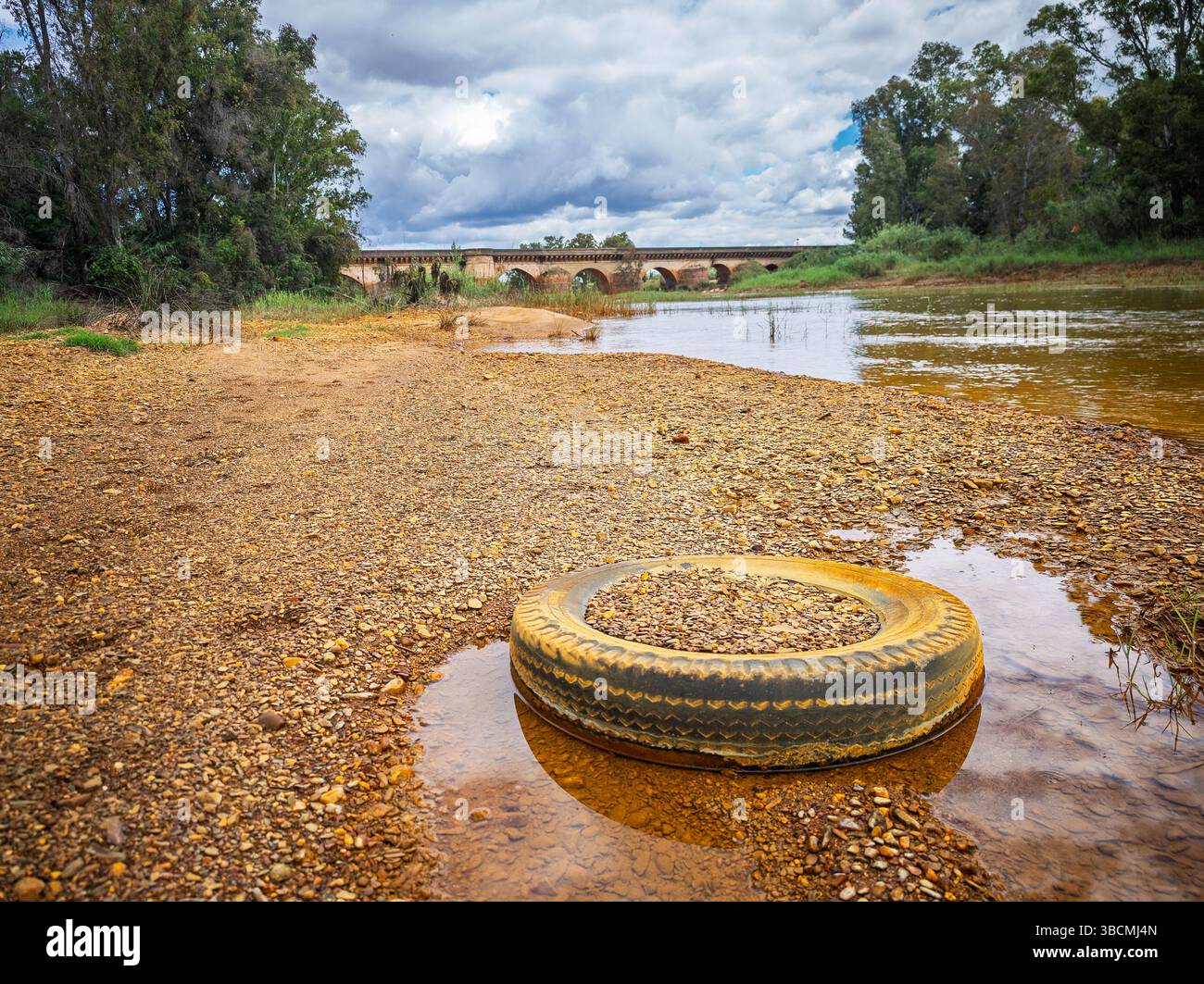Una gomma scartata riposa nelle acque poco profonde del fiume Tinto, evidenziando le sfumature rossastre del paesaggio ricco di minerali di Niebla. Foto Stock