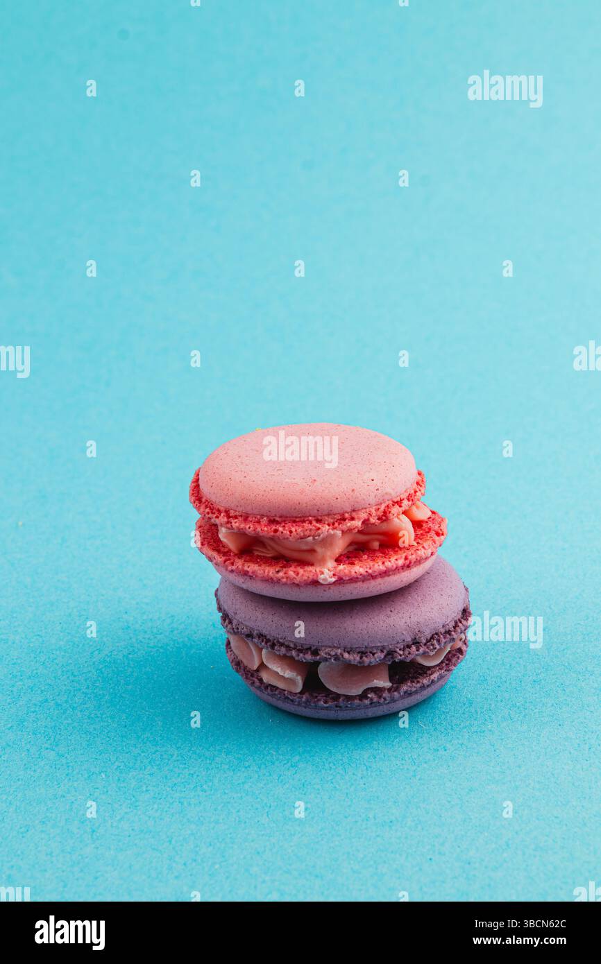 Due macaron, uno rosa e uno viola, sono impilati con cura su una superficie blu brillante, mostrando la loro consistenza liscia e delizioso ripieno, invitino Foto Stock
