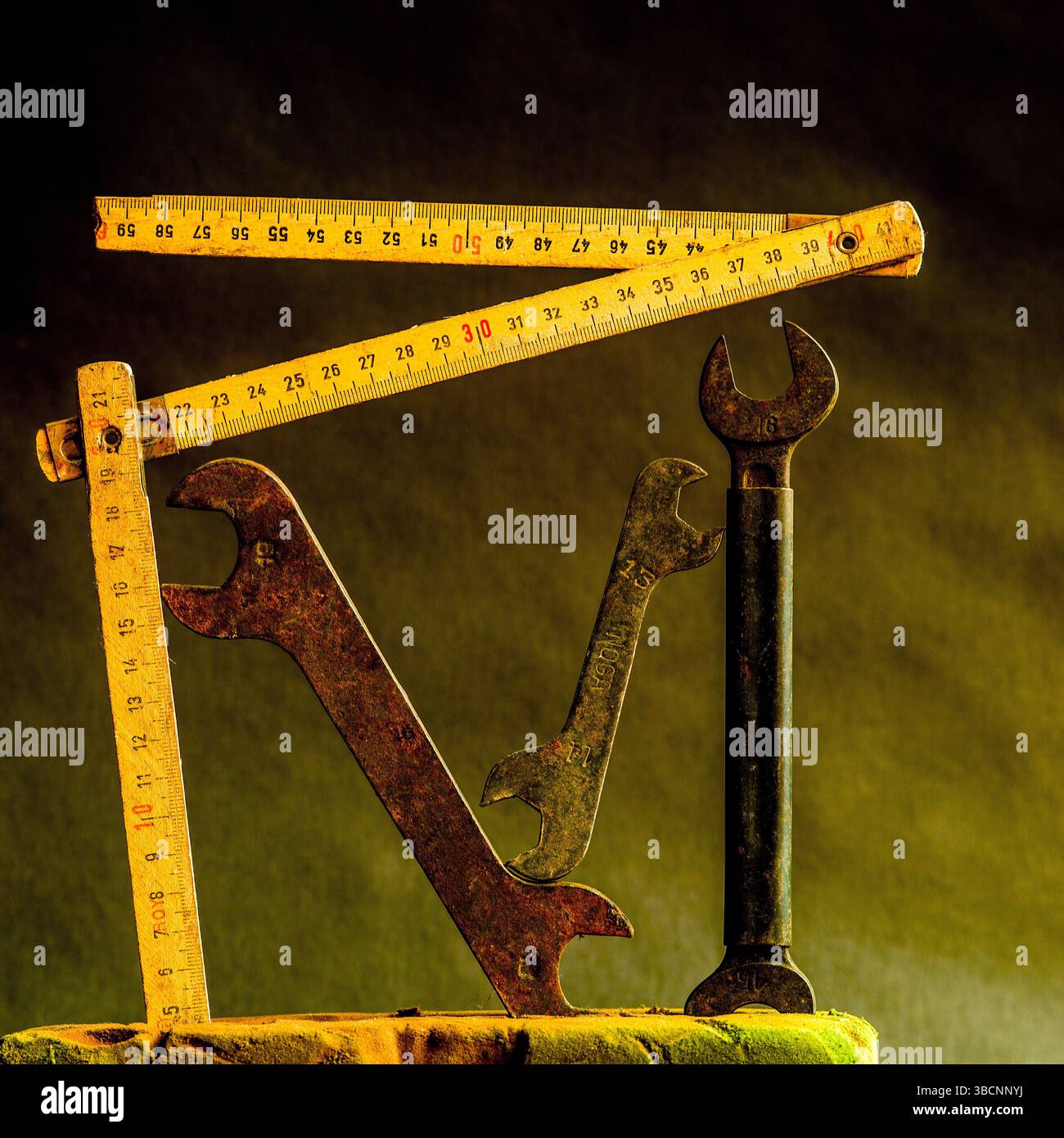 Le chiavi vintage e i metro a nastro in legno sono disposti in modo creativo su uno sfondo scuro e testurizzato, che mette in risalto la bellezza della vecchia artigianalità Foto Stock