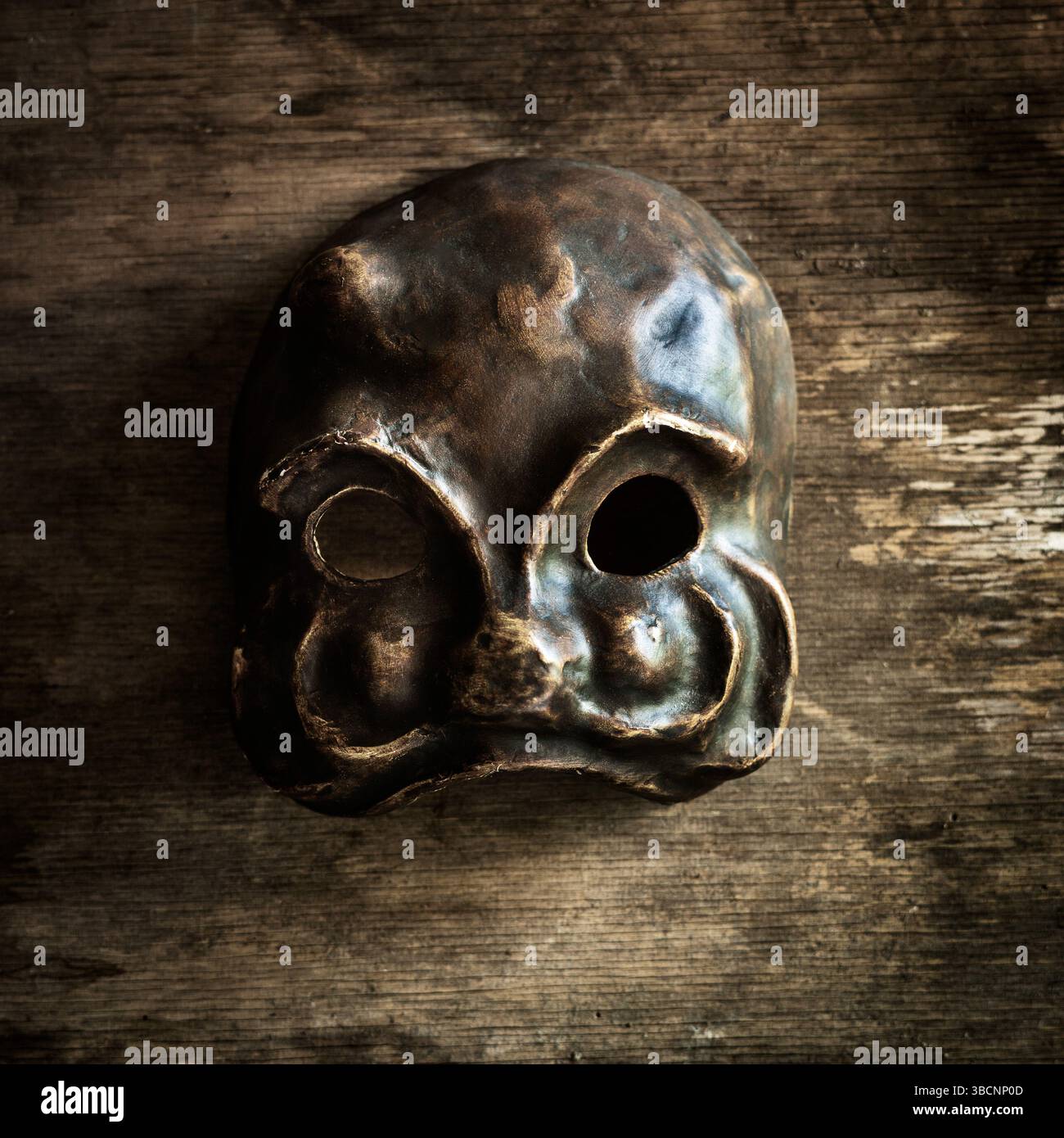 Una maschera cranica artigianale di venezia poggia su una superficie di legno intemprata, evidenziandone la forma e la consistenza uniche. Foto Stock
