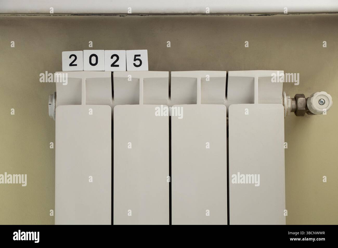 Batteria bianca sotto la finestra nella parete dell'appartamento e cubi con l'anno 2025, sistema di riscaldamento, casa calda Foto Stock