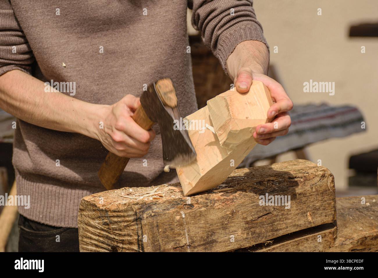 un artigiano lavora su un pezzo di legno con una piccola ascia che forma il legno con strumenti tradizionali Foto Stock