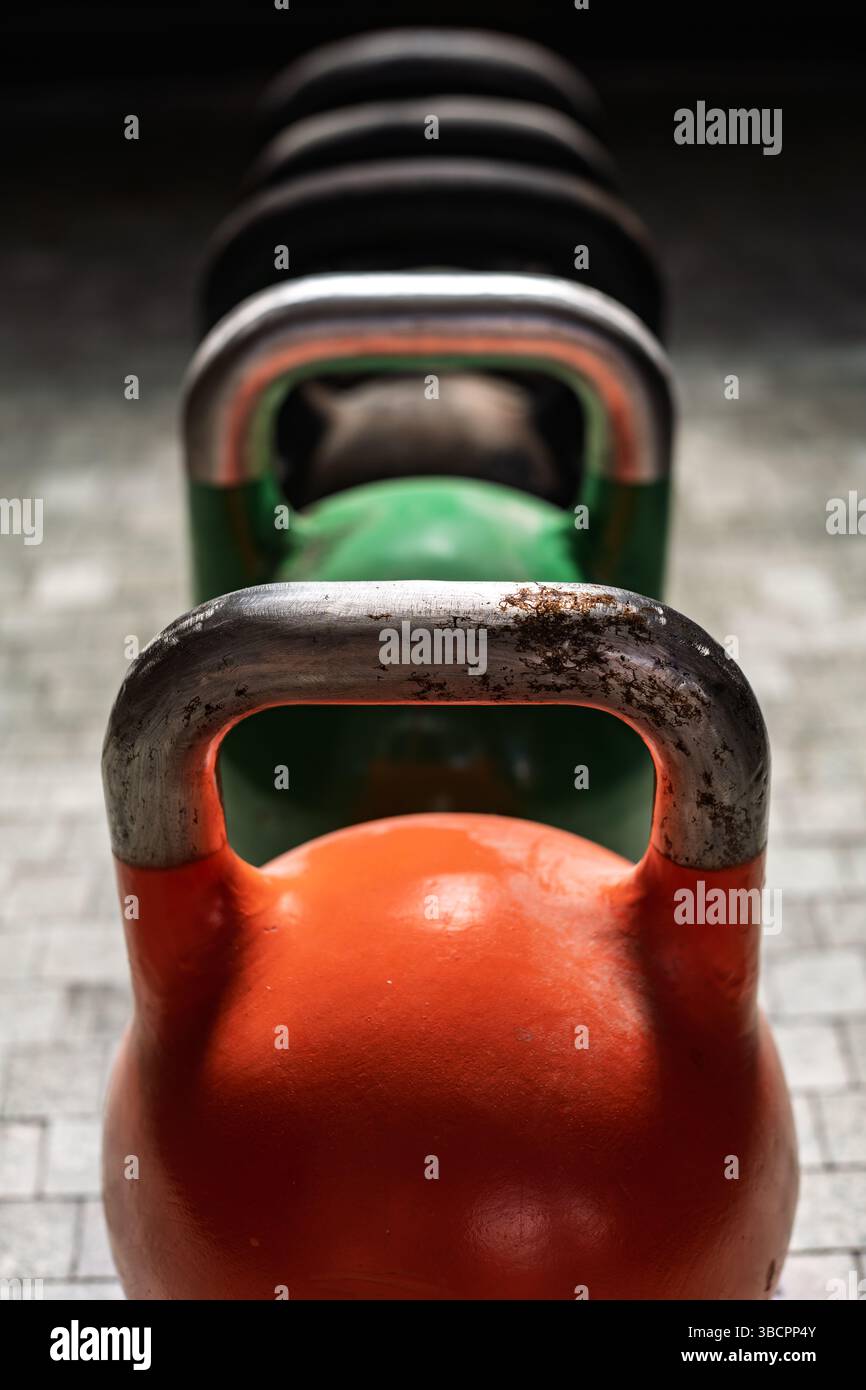 I coloratissimi kettlebell sono allestiti in una sala fitness, pronti per una sessione di allenamento. La luce della sera crea un'atmosfera invitante. Foto Stock