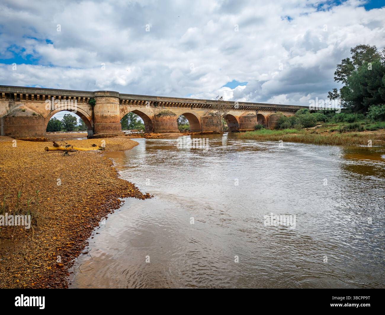 Uno storico ponte romano attraversa il fiume Tinto a Niebla, mostrando il paesaggio naturale e le acque calme sotto un cielo coperto. Foto Stock