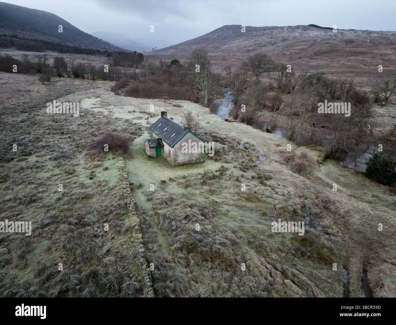Vista aerea di Invermallie Bothy nelle remote Highlands scozzesi, un rifugio di montagna annidato accanto a un fiume tortuoso in un paesaggio selvaggio e ghiacciato Foto Stock