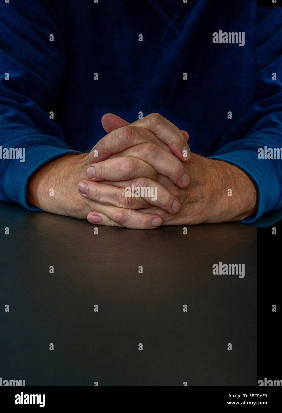 Mani maschili che pregano con mani piegate dita intrecciate viste dalla parte anteriore - scena scura con spazio di copia. Concetto religioso. Foto Stock