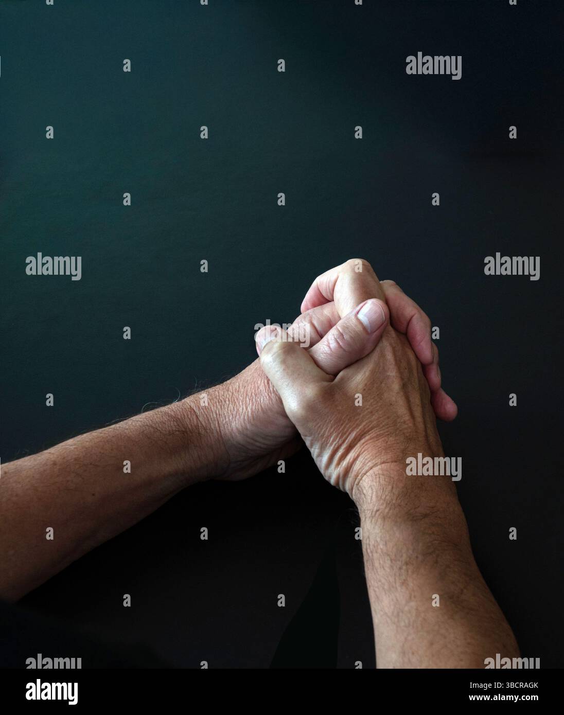 Mani maschili con braccia sottili che pregano con mani piegate dita intrecciate - scena scura con spazio di copia. Concetto religioso. Foto Stock