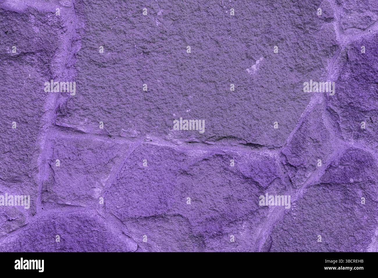 Primo piano di una parete di pietra ruvida dipinta di viola, che mostra la consistenza naturale della roccia e le linee visibili della Malta tra le pietre. Foto Stock