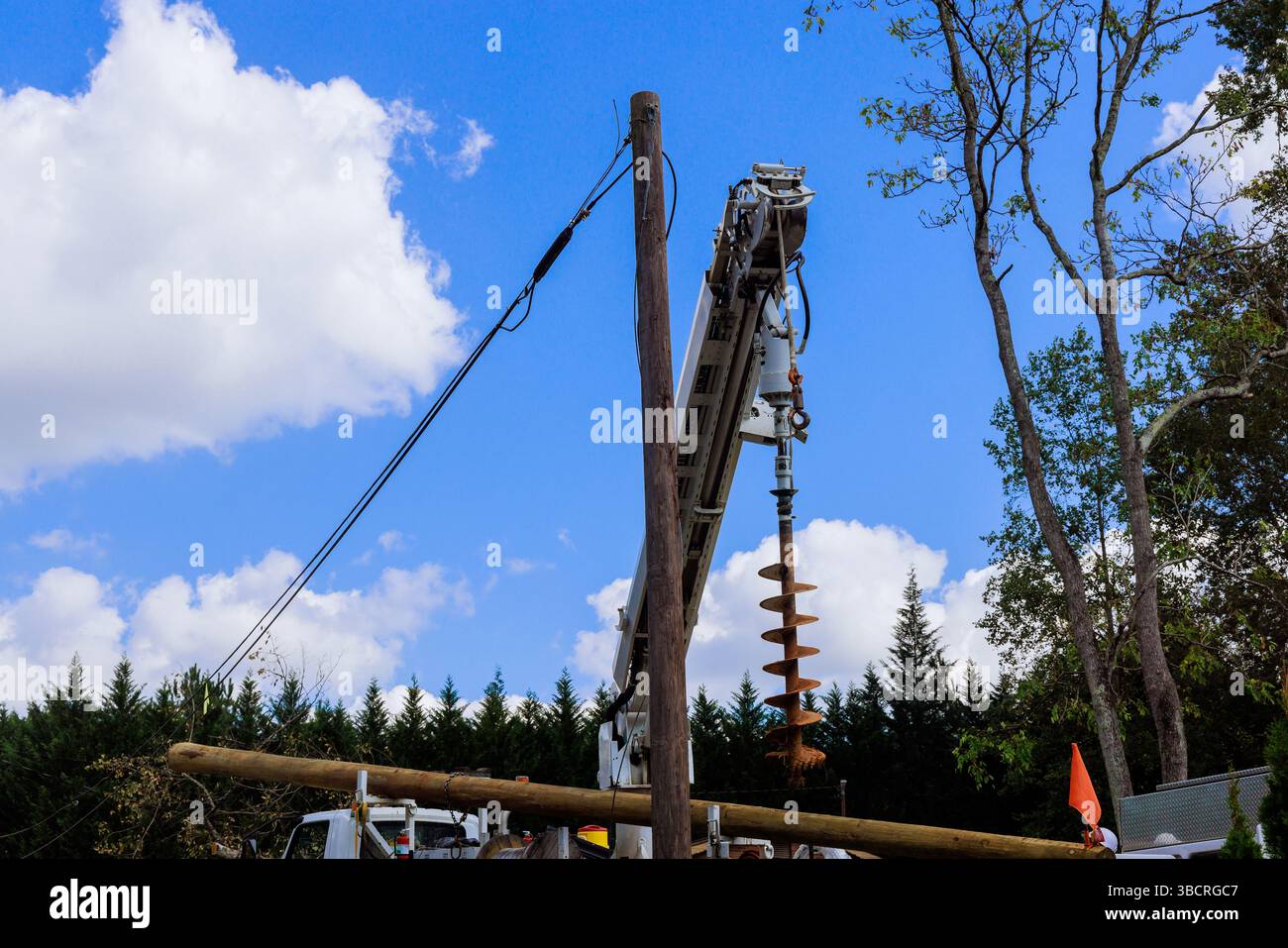 Il personale addetto alle costruzioni utilizza una potente perforatrice a trivella per alesare il terreno in località suburbane durante la riparazione della linea elettrica Foto Stock