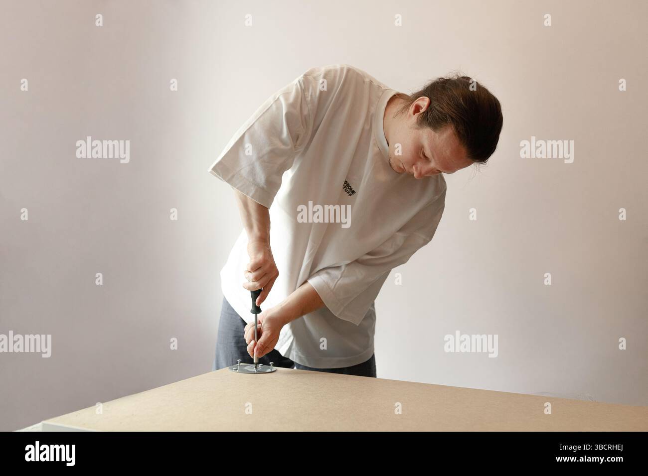 Uomo che si piega per fissare la piastra metallica alla scheda con un cacciavite durante un'attività di assemblaggio a casa. Foto Stock