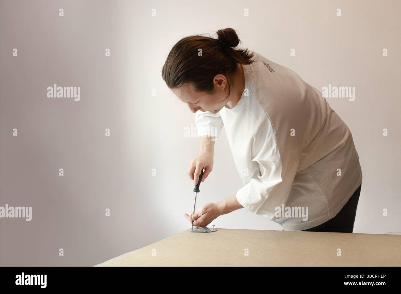 Uomo concentrato in camicia bianca che lavora con un cacciavite per assemblare la staffa in legno e metallo in interni. Foto Stock