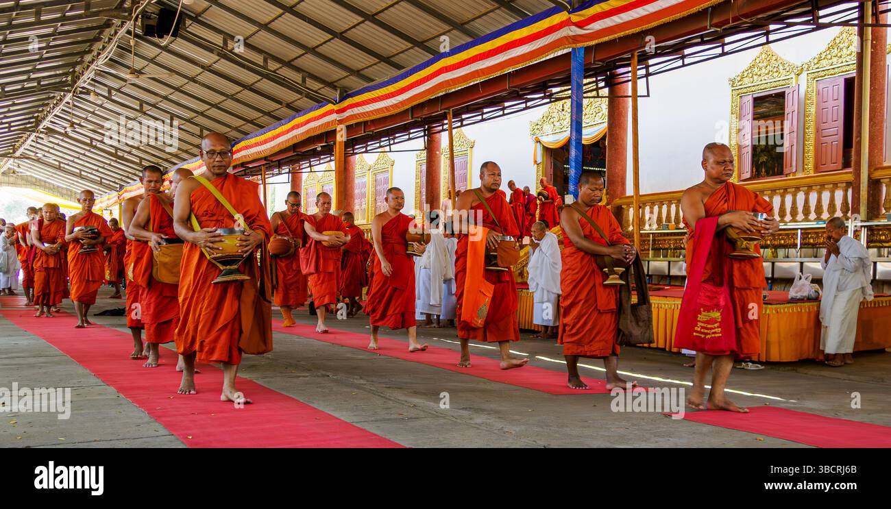 I monaci maschi sfilano con le ciotole per il pranzo fuori dalla sala riunioni per raggiungere a piedi la cucina per ricevere il pranzo al monastero di Udon, in Cambogia Foto Stock