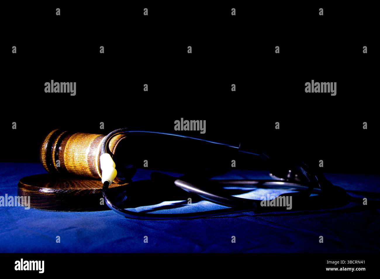 Martelletto e stetoscopio del giudice su un panno blu al buio con retroilluminazione, processo medico in tribunale, legge e giustizia Foto Stock