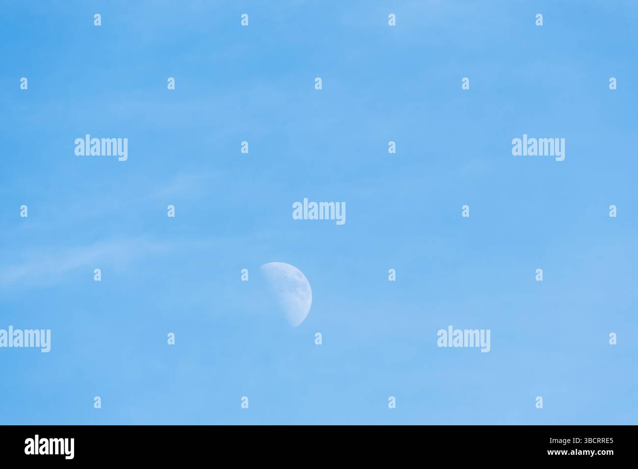 Mezza luna pallida che galleggia con grazia contro il cielo azzurro del giorno Foto Stock