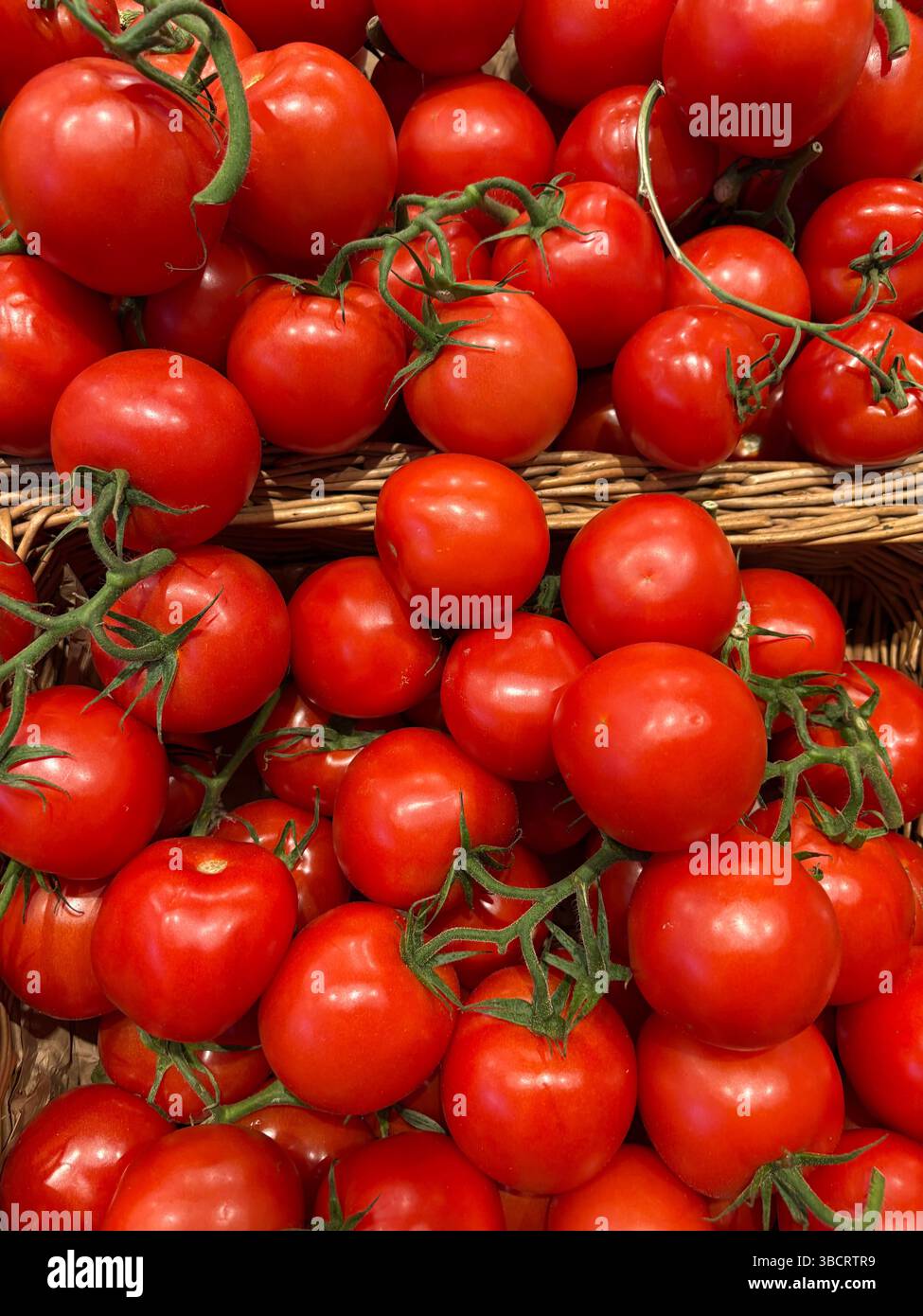 I pomodori rossi brillanti sono disposti in cesti intrecciati in un vivace mercato. I prodotti vibranti sembrano freschi e invitanti, attirando l'attenzione degli acquirenti. Foto Stock